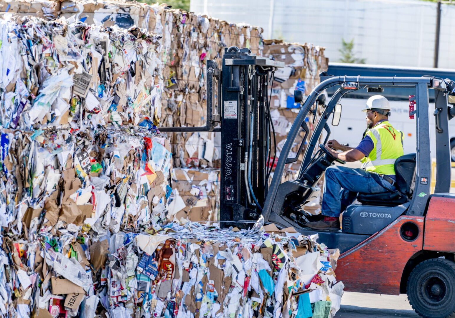 A man driving a forklift in front of a pile of paper.